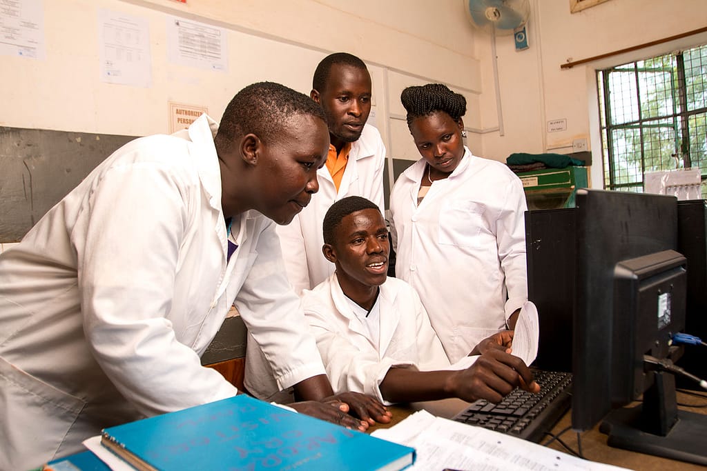 Clinical team wearing white gowns in Africa looking at a computer