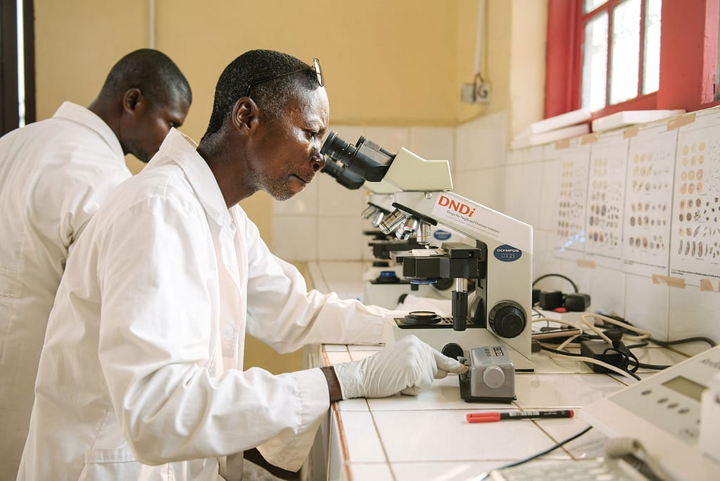 Lab technicians looking into microscope in a clinical working on sleeping sickness
