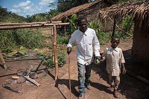 Father walking in rural village with a cane and holding his son's hand